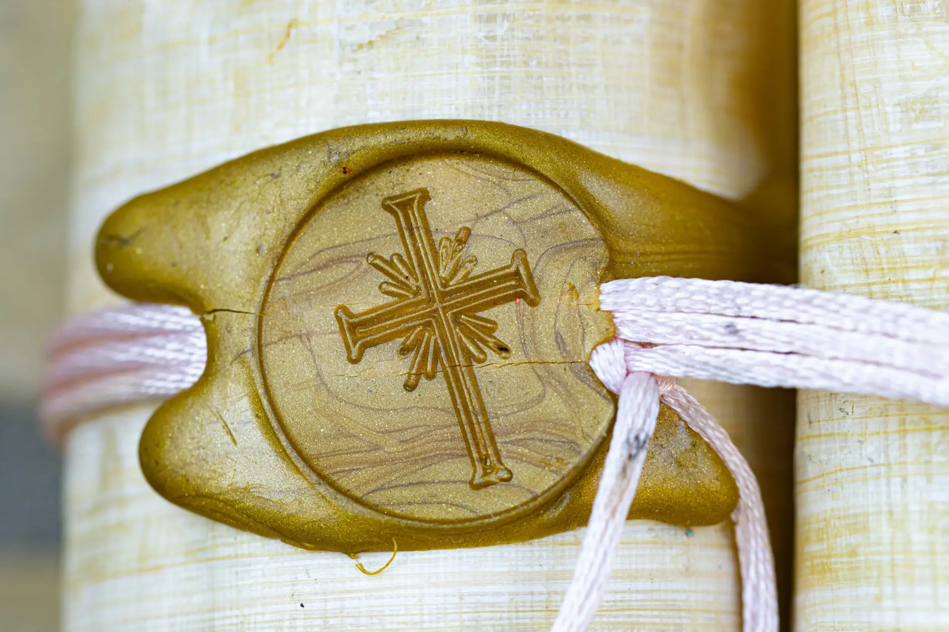 Close-up of a yellow wax seal with a cross design, attached to a rolled parchment related to circumcision and secured with a light-coloured string.