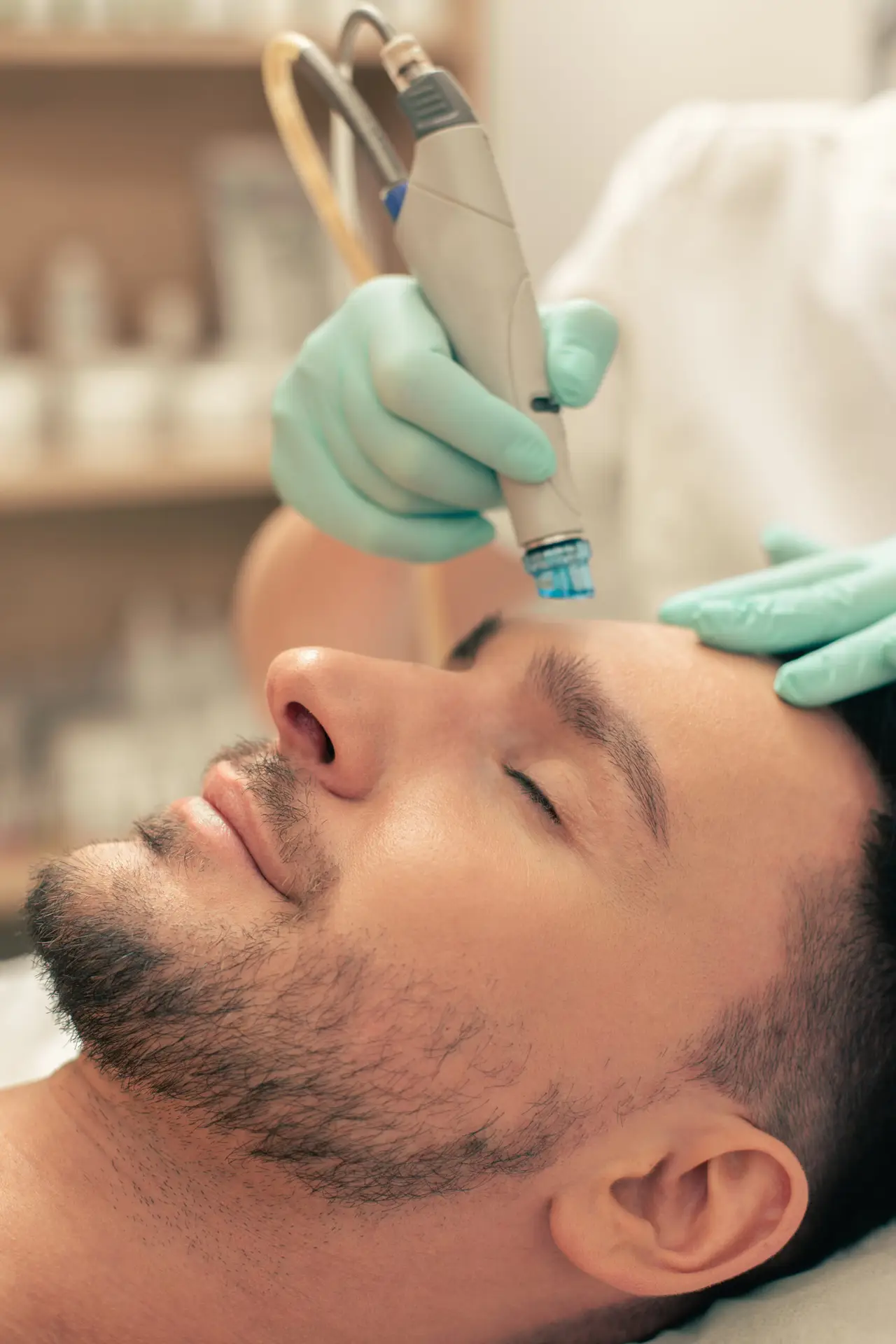 A man with closed eyes receives a facial treatment at a clinic. A gloved professional uses a handheld device on his forehead. The clean, calm setting suggests advanced care, such as anti-wrinkle injections for men in Birmingham.