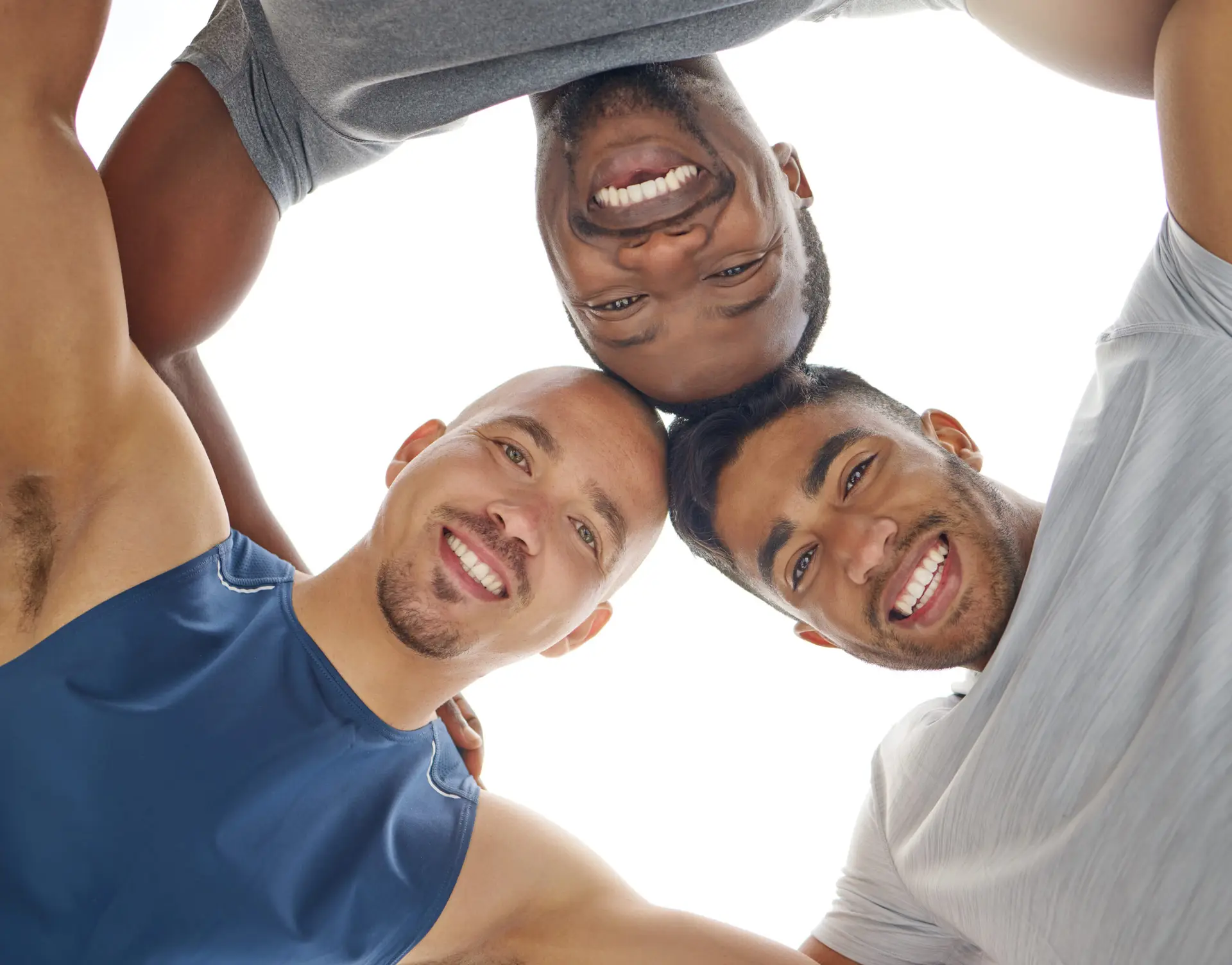 Three men standing close together in a circle, smiling and looking down at the camera with their arms round each other's shoulders against a bright, white background, celebrating friendship after adult circumcision in Birmingham.