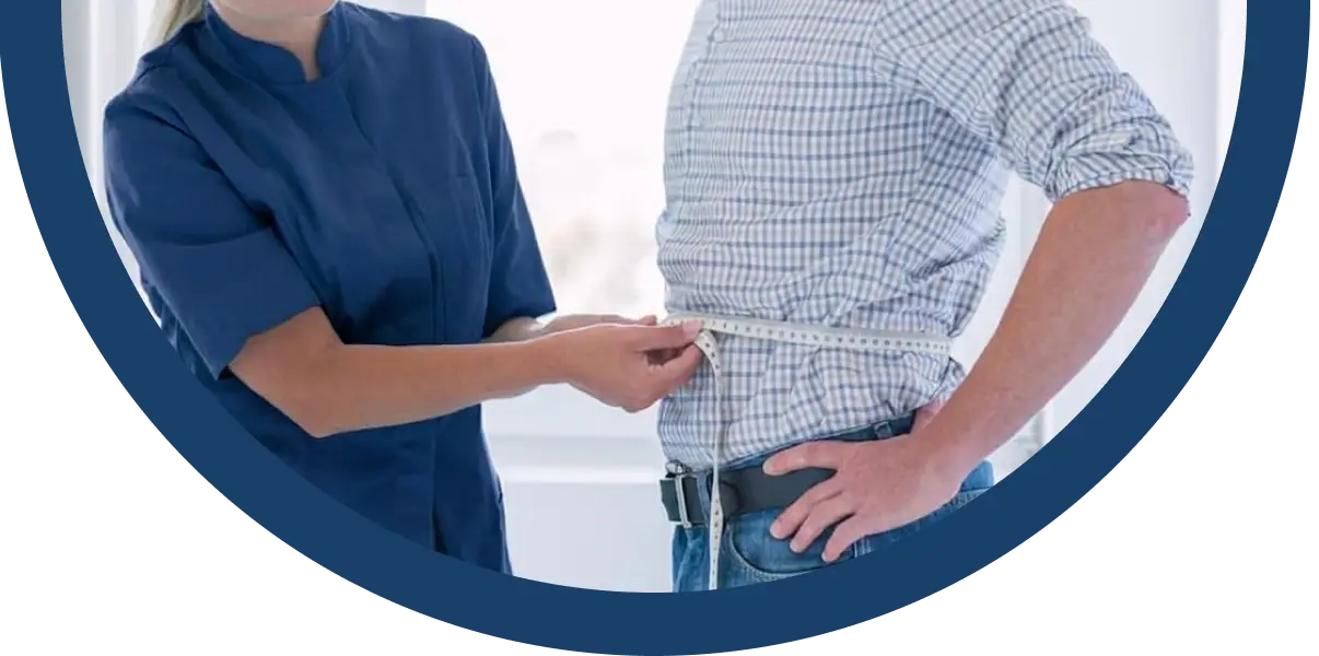 A healthcare professional in a blue uniform measures the waist of a person wearing a checked shirt and jeans with a measuring tape.