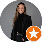 Woman with long brown hair wearing a black polo neck and blazer stands against a grey background. An orange star icon, symbolising awareness related to circumcision, appears in the lower right corner of the image.