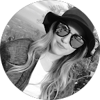 Black and white photo of a woman with long hair wearing a wide-brimmed hat, sunglasses, and a cardigan, smiling at the camera—her joy undimmed as she shares her story about supporting circumcision awareness.