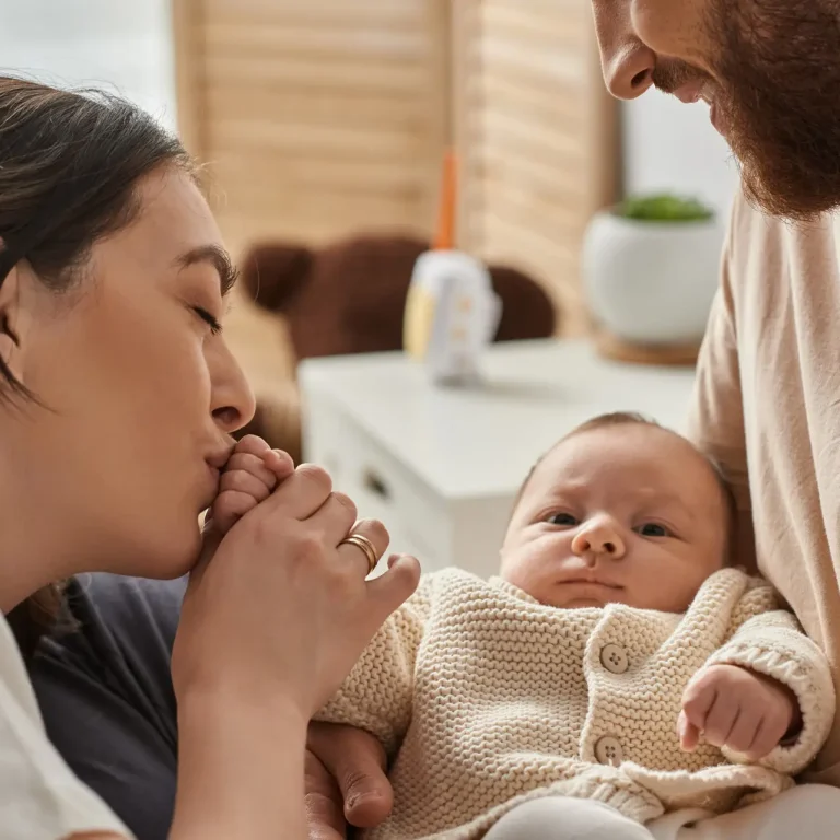 jolly mother kissing little hand of her newborn baby while her husband holding him, family concept