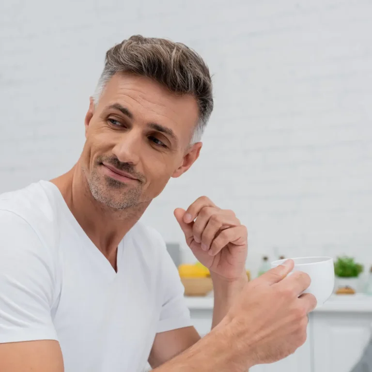 Man in t-shirt holding cup of coffee in kitchen at home